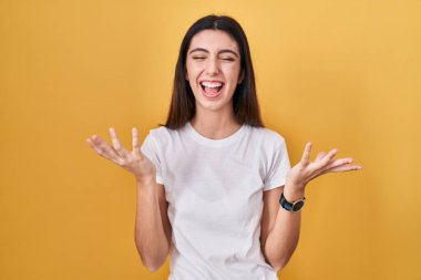 Young beautiful woman standing over yellow background celebrating mad and crazy for success with arms raised and closed eyes screaming excited. winner concept 