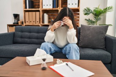 Young hispanic woman patient crying having psychology session at clinic