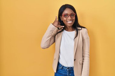 African young woman wearing glasses smiling doing phone gesture with hand and fingers like talking on the telephone. communicating concepts. 