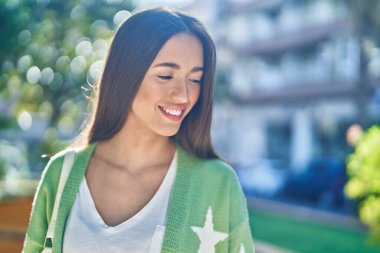 Genç, güzel, İspanyol bir kadın, gülümsüyor. Parkta kendine güveniyor.