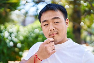 Young chinese man standing with doubt expression at park
