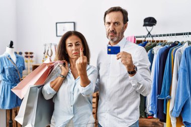 Hispanic middle age couple holding shopping bags and credit card showing middle finger, impolite and rude fuck off expression 