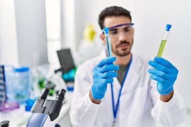 Laboratuvarda test tüpleri tutan bilim adamı üniforması giyen İspanyol bir genç.