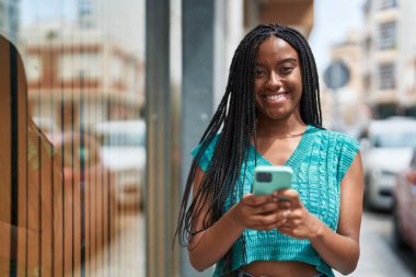 Afro-Amerikalı kadın sokakta akıllı telefon kullanarak kendine güveniyor.
