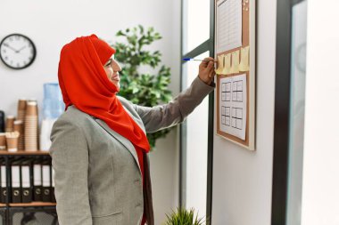 Ofiste mantar panoya Arapça yazan fular takan genç bir kadın.