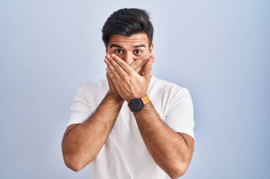 Mavi arka planda dikilen İspanyol adam yanlışlıkla ağzını kapatarak şok geçirdi. gizli kavram. 