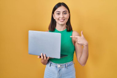 Hispanic girl working using computer laptop pointing finger to one self smiling happy and proud 