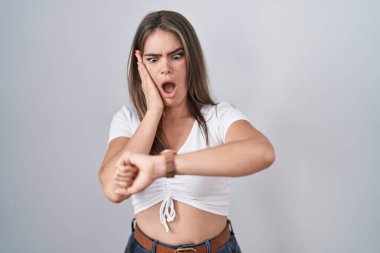 Gayri resmi beyaz tişört giyen genç ve güzel bir kadın saate bakıyor. Endişeli, geç kalmaktan korkuyor. 