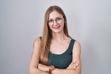 Young caucasian woman standing over white background happy face smiling with crossed arms looking at the camera. positive person. 