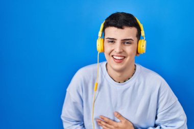 Non binary person listening to music using headphones smiling and laughing hard out loud because funny crazy joke with hands on body. 