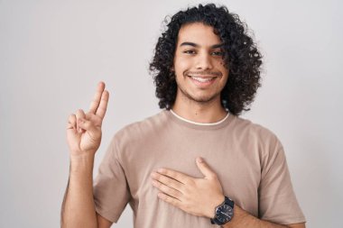 Beyaz arka planda duran kıvırcık saçlı, elleri göğsünde ve parmakları havada küfreden, sadakat yemini eden İspanyol bir adam. 