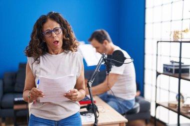 Orta yaşlı İspanyol bir kadın müzik stüdyosunda şok olmuş bir şekilde şarkı söylüyor. Şüpheci ve alaycı görünüyor. 