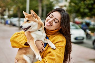 Güzel genç bir kadın sokakta mutlu Shiba Inu köpeğine sarılıyor.