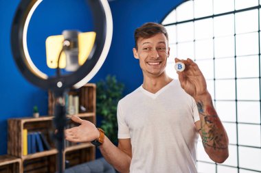 Beyaz adam evde akıllı telefonla Bitcoin dersi kaydediyor başarıyı mutlu bir gülümsemeyle kutluyor ve kazanan el kaldırarak ifade ediyor 