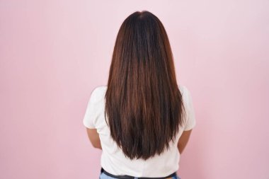 Young brunette woman standing over pink background standing backwards looking away with crossed arms 