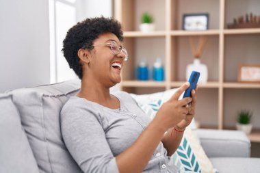 Evdeki koltukta oturan Afro-Amerikan kadın akıllı telefon kullanıyor