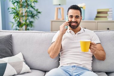 Genç İspanyol adam kahve içiyor ve evde akıllı telefondan konuşuyor.