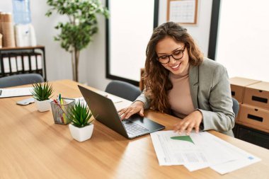 Young beautiful hispanic woman business worker using laptop reading document at office