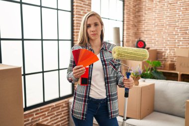 Yeni evinde patenci boyacısı ve boya örnekleri tutan genç sarışın kadın depresyonda ve endişe içinde, kızgın ve korkmuş bir şekilde ağlıyor. hüzünlü ifade. 