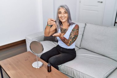 Orta yaşlı, kır saçlı, gülümseyen, elinde serum tutan bir kadın.