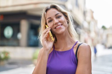 Genç sarışın kadın gülümsüyor. Kendine güveni tam. Akıllı telefondan konuşuyor.