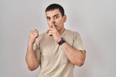 Young arab man wearing casual t shirt asking to be quiet with finger on lips pointing with hand to the side. silence and secret concept. 
