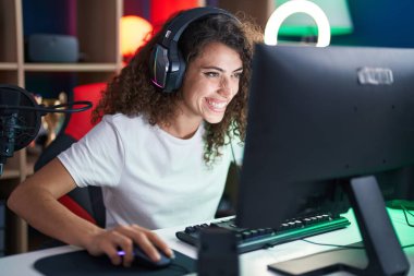 Young beautiful hispanic woman streamer playing video game using computer at gaming room