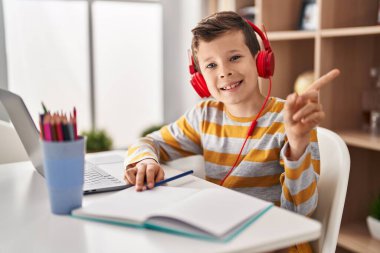 Genç beyaz çocuk evde ödev yapıyor gülümsüyor mutlu bir şekilde el ve parmak kenarı işaret ediyor. 