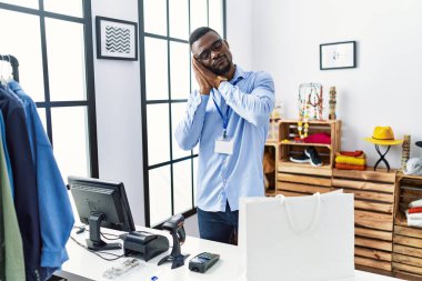 Young african man working as manager at retail boutique sleeping tired dreaming and posing with hands together while smiling with closed eyes. 