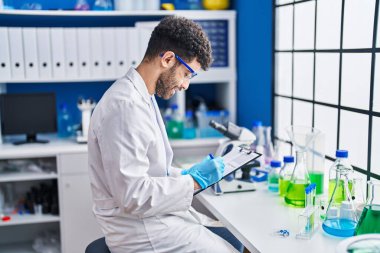 Laboratuvarda panoya yazan bilim adamı üniforması giyen genç bir Arap.