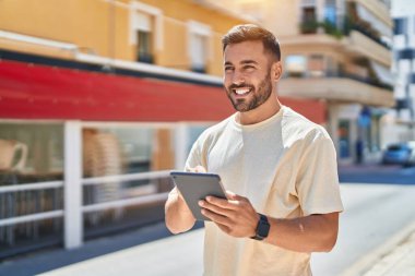 Young hispanic man smiling confident using touchpad at street