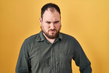 Plus size hispanic man with beard standing over yellow background skeptic and nervous, frowning upset because of problem. negative person. 