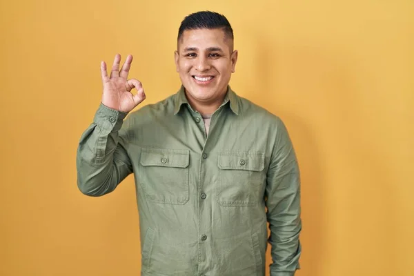 黄色の背景の上に立つヒスパニック系の若い男は手と指でOkサインを行う積極的な笑顔 成功した表現 — ストック写真