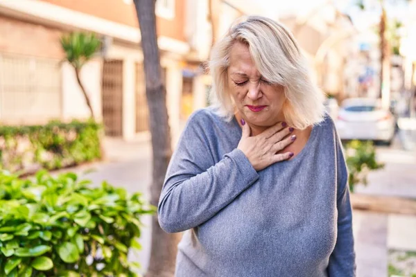 Middle age blonde woman coughing at street