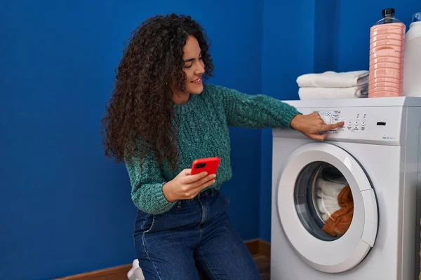 年轻美丽的惊慌失措的女人在洗衣房用智能手机打开洗衣机 — 图库照片