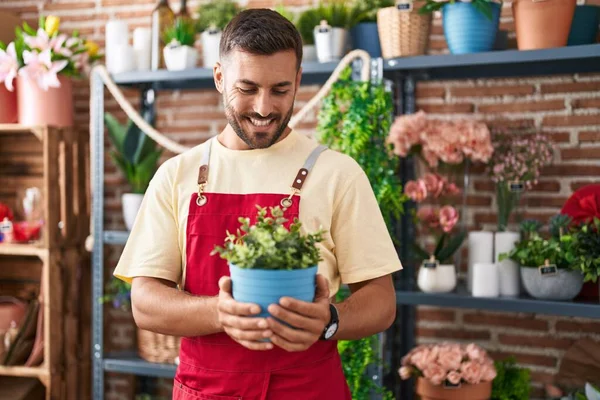 Young hispanic man florist smiling confident holding plant at florist