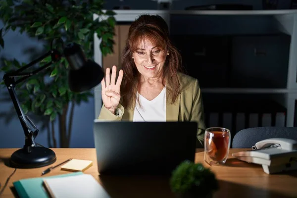 中年时 他的惊慌失措的女人在晚上用电脑笔记本电脑工作 带着自信和快乐的笑容 用手指指指着四号 — 图库照片