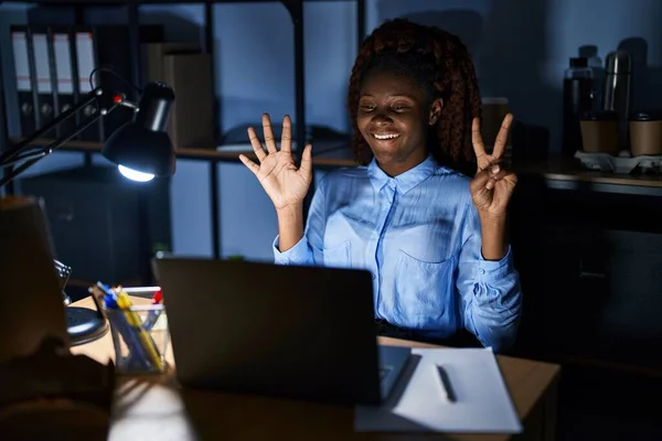 African woman working at the office at night showing and pointing up with fingers number seven while smiling confident and happy.