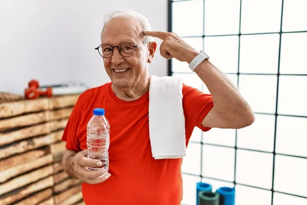 Senior man wearing sportswear and towel at the gym smiling pointing to head with one finger, great idea or thought, good memory