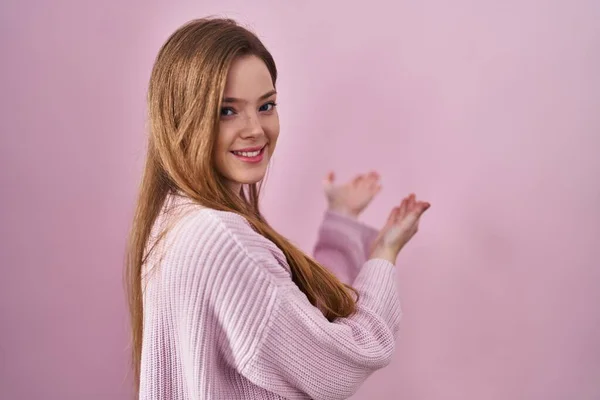 年轻的高加索女人站在粉色的背景上 用张开的手自然地微笑着走进来 — 图库照片