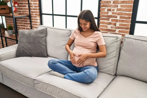 Młoda Latynoska Kobieta Ciąży Dotyka Brzucha Siedząc Kanapie Domu — Zdjęcie stockowe