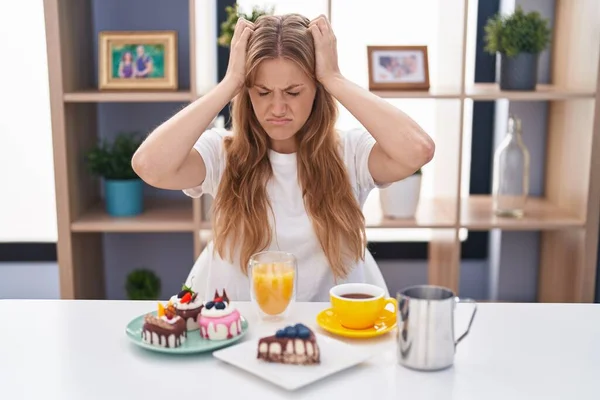 痛みや片頭痛のため 若い白人女性は必死に頭痛やストレスに苦しんで朝食のペストリーを食べています 手を頭に — ストック写真