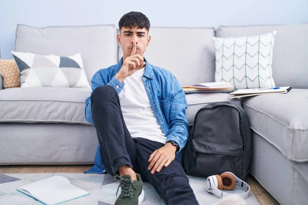 Young Hispanic Man Sitting Floor Studying University Asking Quiet Finger — Zdjęcie stockowe