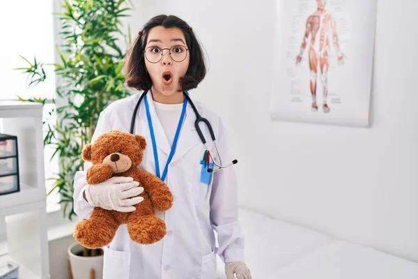 Young Hispanic Doctor Woman Holding Teddy Bear Scared Amazed Open — Stok fotoğraf