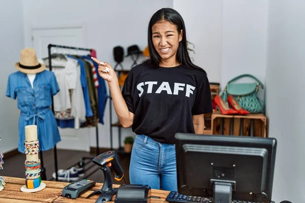 Young hispanic woman working as staff at retail boutique pointing aside worried and nervous with forefinger, concerned and surprised expression
