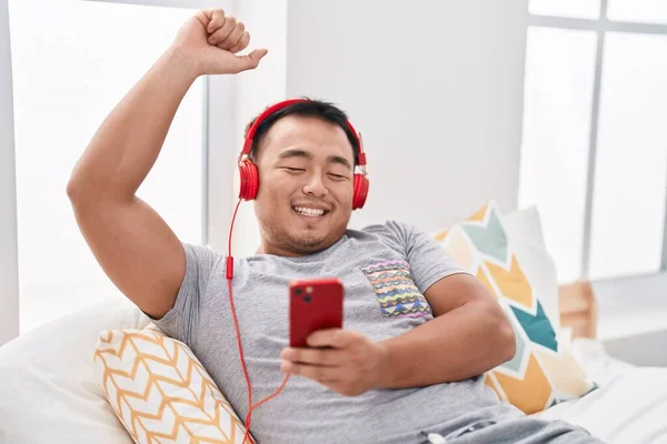 Young chinese man listening to music lying on bed at bedroom