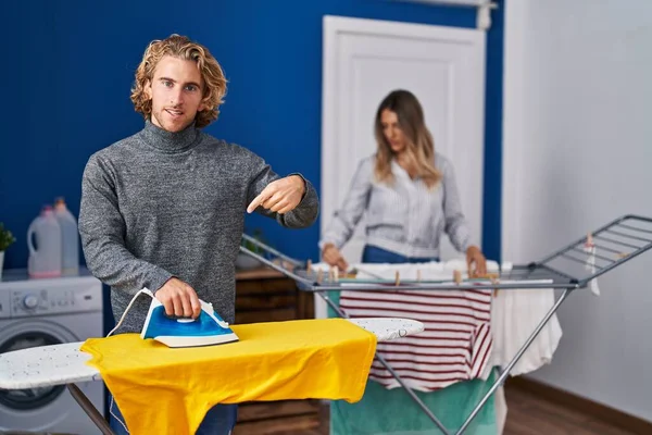 Couple ironing clothes at laundry room smiling happy pointing with hand and finger