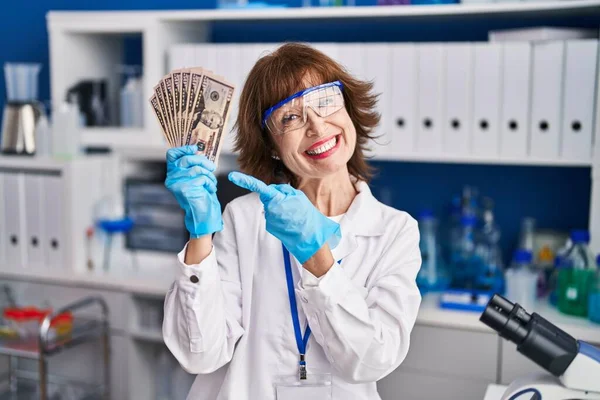 在科学家实验室工作的中年妇女微笑着拿着钱 高兴地用手和手指指指点点 — 图库照片
