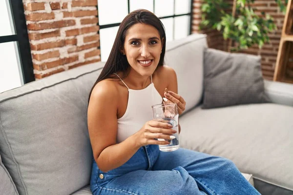 Mujer Hispana Joven Tomando Píldora Bebiendo Agua Sentada Sofá Casa — Foto de Stock
