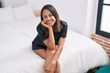 Genç İspanyol kadın yatakta kendinden emin bir şekilde gülümsüyor.